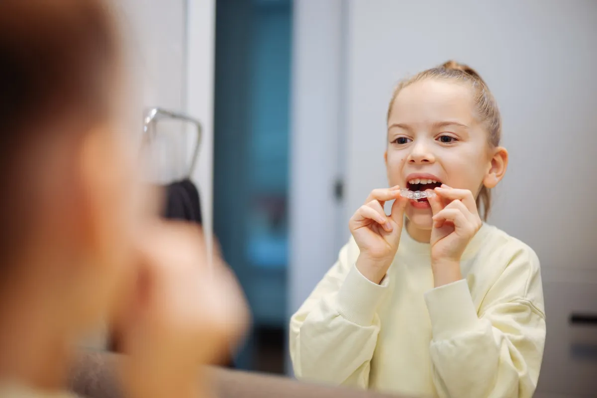 A young girl placing a clear aligner in front of a mirror