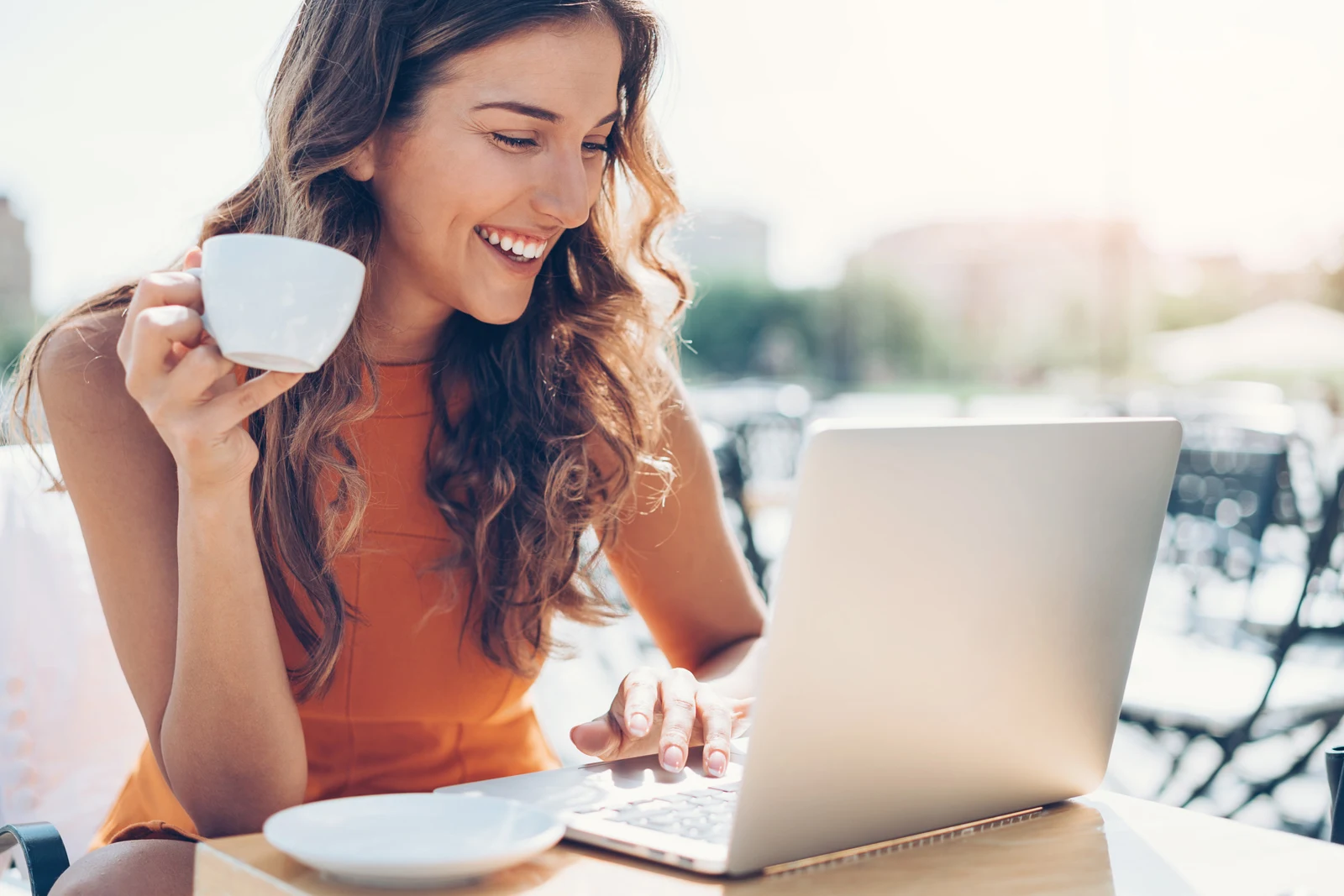 A woman smiling while reaching out from a sunlit outdoor cafe